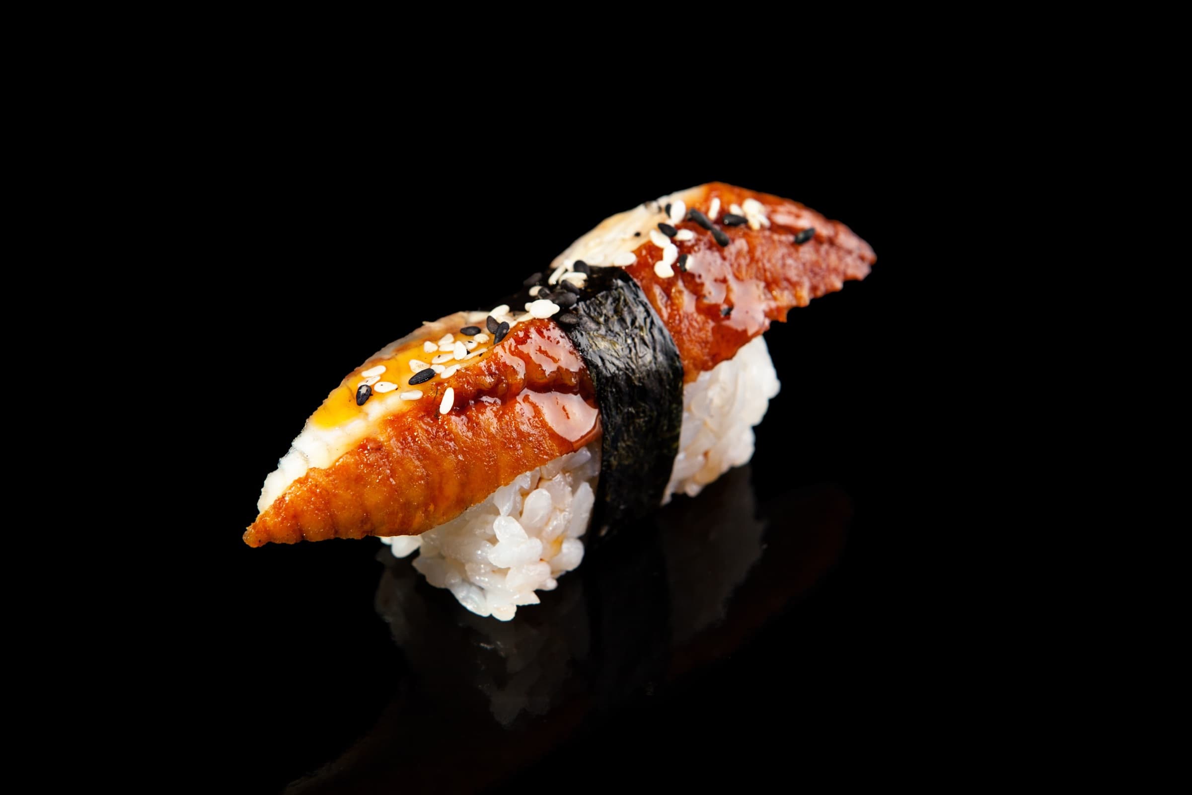 Nigiri de anguila glaseada con sésamo sobre fondo negro